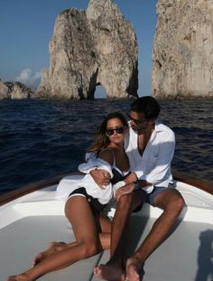 a man and woman sitting on the bow of a boat in front of rock formations