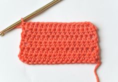 an orange crochet stitch is next to a knitting needle