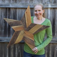 a woman holding a wooden star in front of a fence with wood slats on it