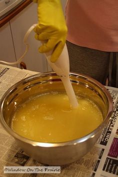 a person in yellow gloves pours liquid into a silver bowl on top of a newspaper