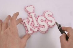 someone is cutting out the word kiss on a piece of cake that says kiss in white and pink polka dots