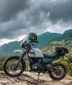 a motorcycle parked on top of a dirt hill with mountains in the backgroud