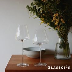 two wine glasses sitting on top of a wooden table next to a vase filled with flowers