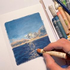 a person is drawing with colored pencils and watercolors on a white paper