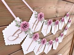 some paper flowers are hanging on a wooden wall and there is a sign with the letter b