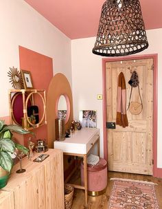 a room with pink walls and wooden floors has a desk, chair, mirror, rug and hanging light fixture