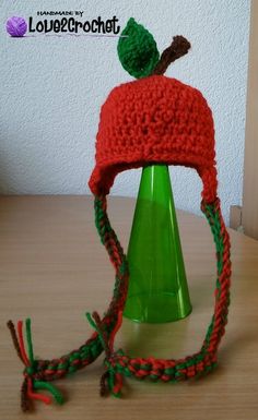 a red knitted hat with a green plastic cup underneath it on top of a wooden table