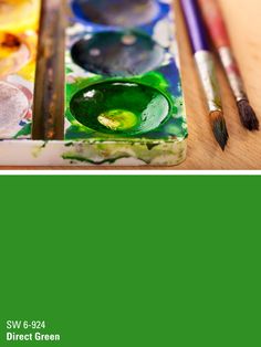 some paint and brushes sitting on top of a wooden table in front of a green background