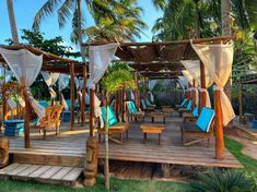 a wooden deck with chairs and umbrellas on it next to palm trees in the background