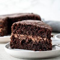 a piece of chocolate cake on a plate with a fork next to it and another slice in the background