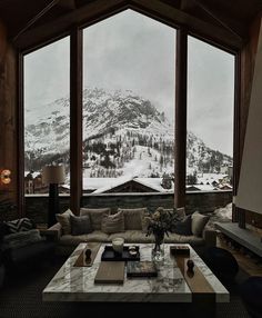 a living room filled with furniture and a large window overlooking a mountain covered in snow