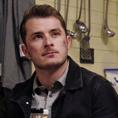 a man sitting at a table with a beer in front of him and spoons hanging on the wall behind him