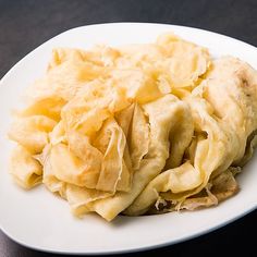 a white plate topped with pasta on top of a black table next to a knife and fork