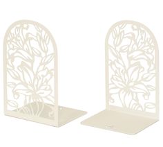 two white metal bookends with floral designs on each side and one holding a card holder