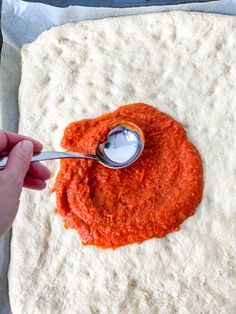 someone is spreading sauce on top of an uncooked tortilla shell with a spoon