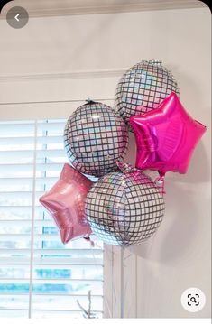 some pink and silver balloons are hanging on the wall in front of a window with shutters