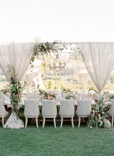 an outdoor wedding setup with white chairs and greenery on the table, surrounded by flowers