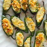 stuffed green peppers topped with cheese and seasoning sit on a white plate, ready to be eaten