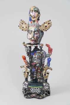 a statue made out of various objects on a white surface with one person's head in the middle