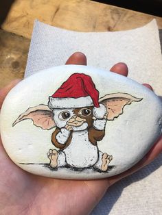 a hand holding a rock with an image of a baby grember wearing a santa hat