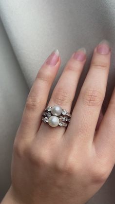 a woman's hand wearing a ring with pearls and diamonds on the middle finger