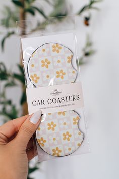 a package of car coasters with yellow flowers on the front and white background, in someone's hand