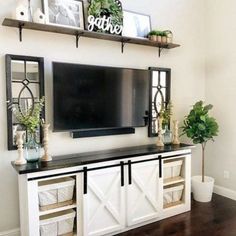 a tv mounted on top of a wooden shelf next to a white cabinet and potted plants