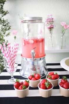 some strawberries are sitting in small cups on a table with a beverage dispenser