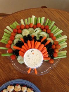 a platter filled with veggies, cucumbers, carrots and dip