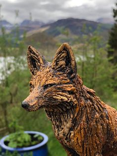 a close up of a statue of a dog with trees in the back ground and mountains in the background