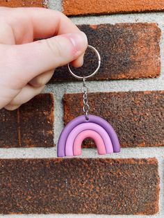 a hand holding a keychain that has a rainbow on it and a brick wall in the background