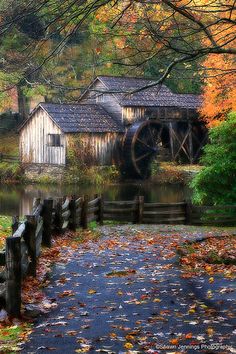 an old mill in the fall with leaves on the ground next to it and water