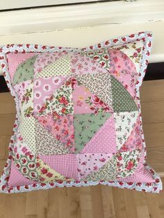 a pink and green patchwork pillow sitting on top of a wooden floor next to a window