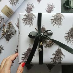 a person holding a wrapped present in front of wrapping paper with pine trees on it