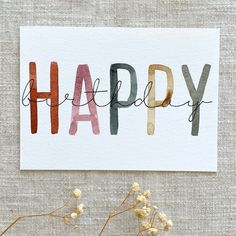 a card with the word happy written in multicolored letters on it next to some flowers