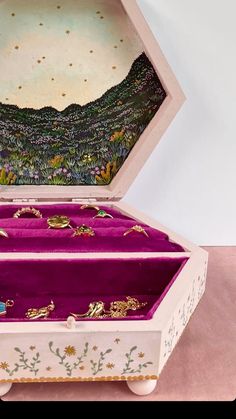 an open jewelry box sitting on top of a pink table next to a white wall