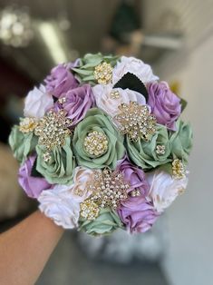 a bridal bouquet with purple, green and white flowers is being held by someone's hand