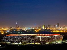 an aerial view of a stadium at night with the city lights in the back ground