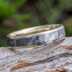 a yellow gold wedding band with black and white marble inlays on a rock