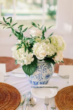 white flowers in a blue and white vase on a table with place settings for two