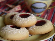 three powdered sugar cookies on a plate with jam in the middle and coffee mug behind them