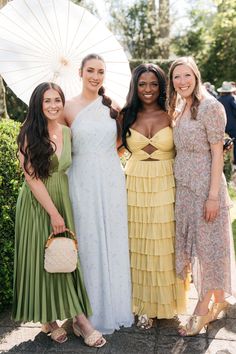 three women standing next to each other in dresses and holding an open white parasol