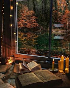 an open book sitting on top of a table next to two candles and a window