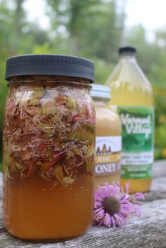 a jar filled with flowers sitting on top of a wooden table next to two bottles