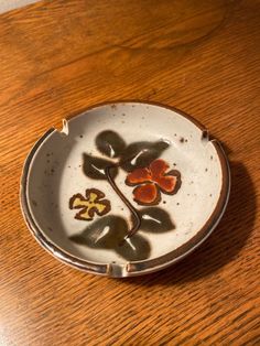 a white plate with flowers painted on it sitting on a wooden table next to a cup