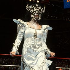 a woman in a white dress standing on top of a wrestling ring wearing a mask