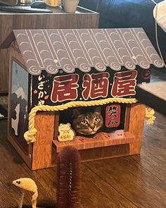 a cat is hiding in a dollhouse made out of wood and paper with chinese characters on the roof