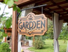 a wooden sign hanging from the side of a building next to a lush green field