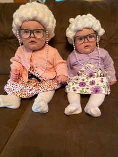 two baby dolls sitting on top of a couch next to each other, wearing glasses