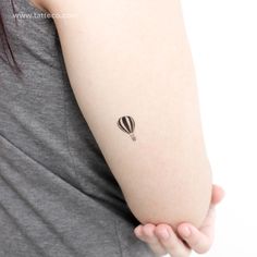 a woman's arm with a small hot air balloon tattoo on her left arm